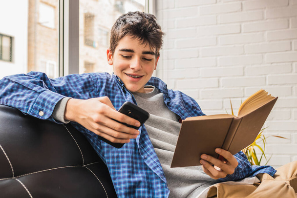 mladý dospívající chlapec s mobilním telefonem a knihy doma nebo v bytě - Fotografie, Obrázek