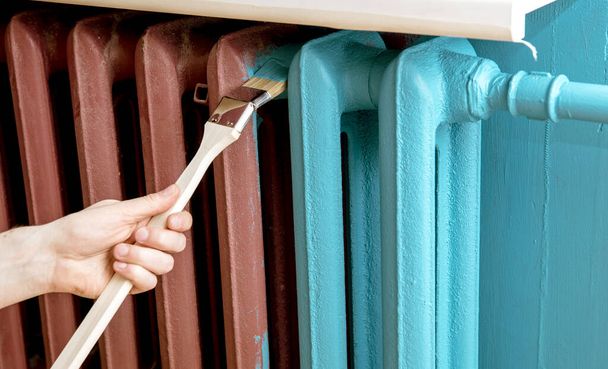 Home refreshing renovation concept. Close up view of man hand painting with special curved radiator paint brush. - Photo, Image