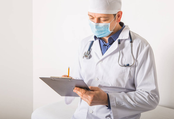 Doctor  in mask with stethoscope writing RX prescription on clipboard on white background, closeup. Medical service - Foto, imagen