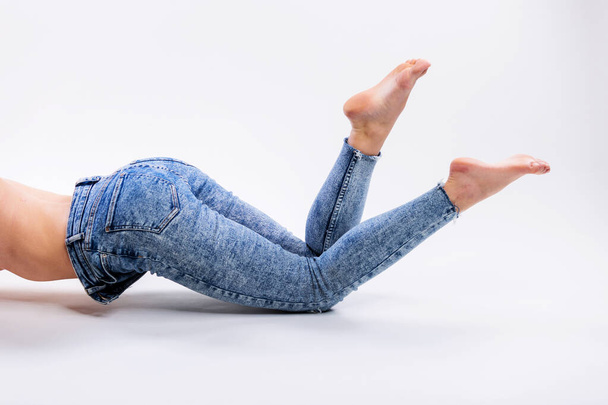 Close up of a beautiful woman legs in blue jeans and barefoot isolated on a gray background - Фото, изображение