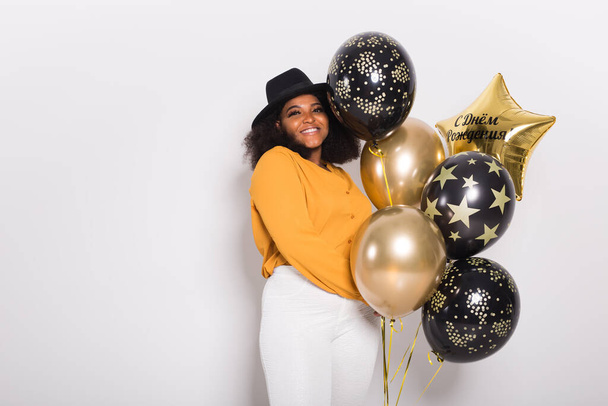Urlaub, Geburtstagsparty und Spaßkonzept - Porträt einer lächelnden jungen Afroamerikanerin, die stilvoll auf weißem Hintergrund mit Luftballons aussieht. - Foto, Bild