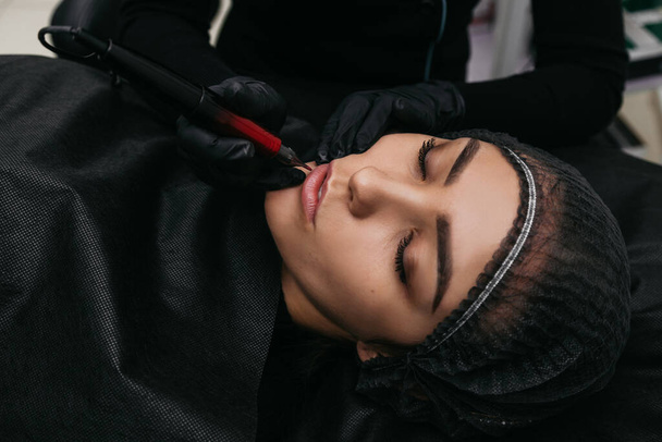 A professional master cosmetologist makes lip tattoo on a pigment. Macro close-up shot - Foto, Imagen