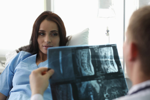 Patiënt liggend op bed kijkend naar dokter met röntgenfoto - Foto, afbeelding