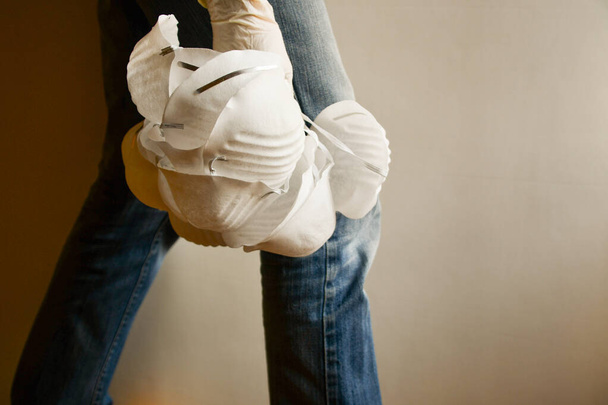 Chica en jeans con muchas máscaras quirúrgicas blancas colgando en la mano con guante de látex desechable
 - Foto, imagen