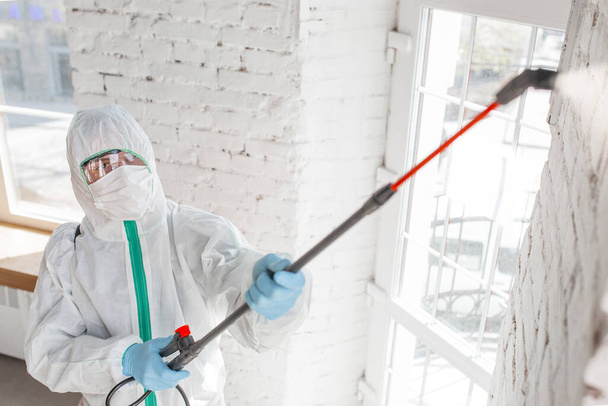 Coronavirus Pandemic. A disinfector in a protective suit and mask sprays disinfectants in the house or office - Foto, imagen