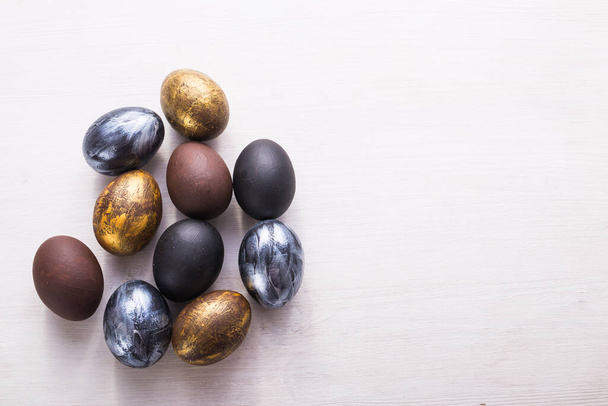 Ünnepek, hagyományok és húsvéti koncepció - Sötét, stílusos húsvéti tojás fehér fából készült háttérrel, másolótérrel. - Fotó, kép
