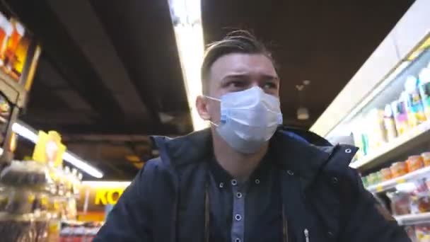 Πορτρέτο του νεαρού άνδρα με ιατρική μάσκα προσώπου περπάτημα στο σούπερ μάρκετ. Ένας τύπος που πηγαίνει στο μαγαζί με προστατευτική μάσκα από τον ιό. Ψώνια στο παντοπωλείο κατά τη διάρκεια πανδημίας του κορωνοϊού. Έννοια της υγείας. COVID-19 - Πλάνα, βίντεο