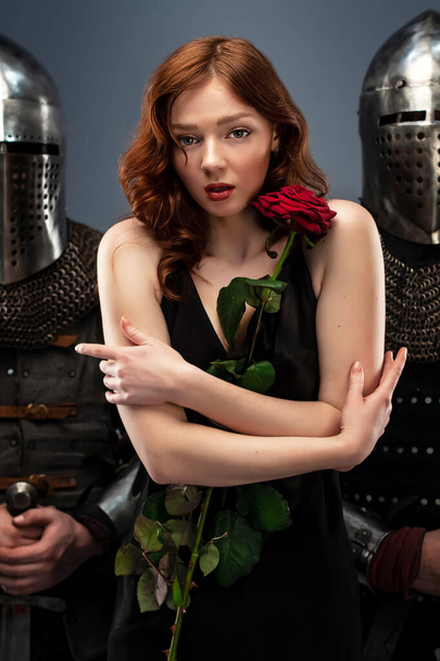 黒のドレスを着た美しい女の子と赤いバラ彼女の手鎧の2つの騎士の横に - 写真・画像