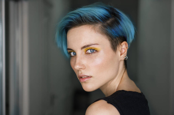 Portré af egy lány kék haj és sárga szem smink egy szépségszalonban előtt egy gyűrű fény kék fényes háttér. Vízszintes lövés. Közelkép - Fotó, kép