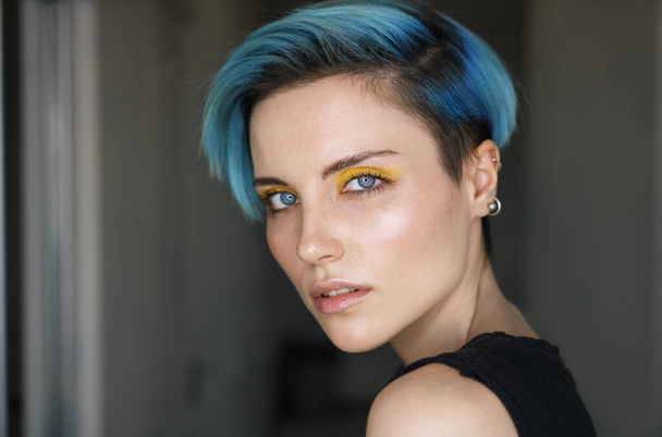 Retrato af uma menina com cabelo azul e maquiagem olho amarelo em um salão de beleza na frente de um anel de luz no fundo azul brilhante. Tiro horizontal. Close-up
 - Foto, Imagem