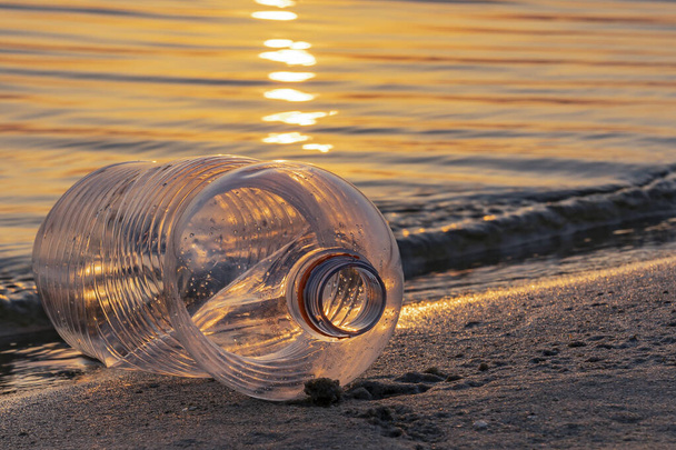 Gün batımında Hollanda, Zoetermeer 'deki Zoetermeerse Plas Gölü kıyısındaki boş bir plastik şişe boyunca alçak güneş parlar. - Fotoğraf, Görsel