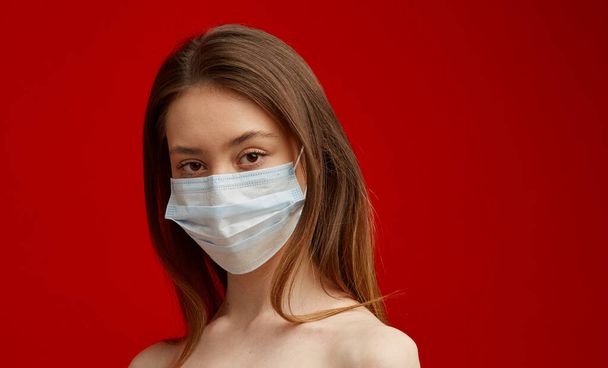 A young girl in a medical mask on a red background. Poster about the coronavirus COVID-19 pandemic. - Fotoğraf, Görsel