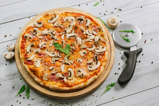 Tasty pizza Caprizzioza with tomato sauce, ham and champignons on the white wooden background - Fotó, kép