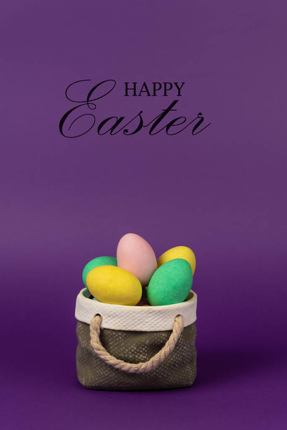 Colorful easter eggs with ceramic basket concept. Text Happy Easter on purple background. - Foto, Imagem