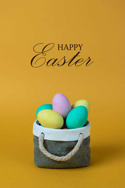 Kolorowe pisanki z ceramiczną koncepcją koszyka. Tekst Happy Easter na pomarańczowym tle. - Zdjęcie, obraz