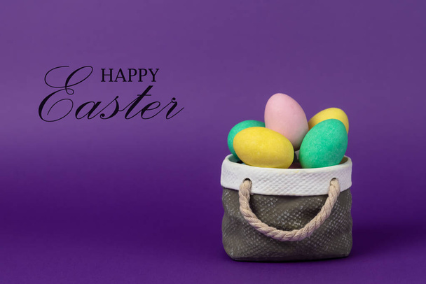 Huevos coloridos de Pascua con concepto de cesta de cerámica. Texto Feliz Pascua sobre fondo púrpura
. - Foto, imagen