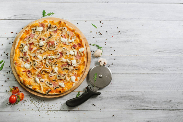 Tasty pizza with mozzarella, hum, chicken fillet, and champingnons on the white wooden background - Photo, Image