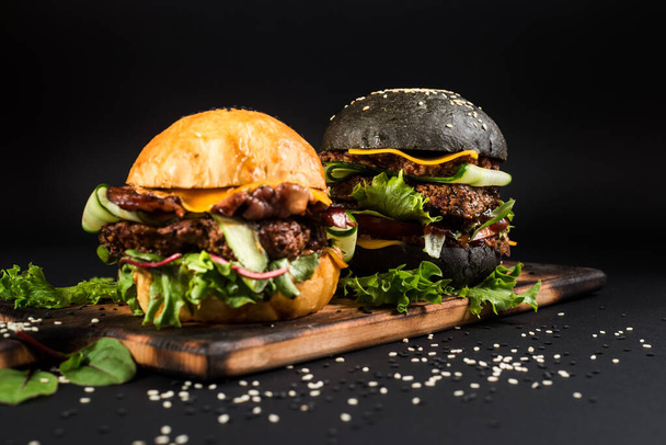 Tasty burgers with black and white bun on wooden desk on the black background - Foto, Bild