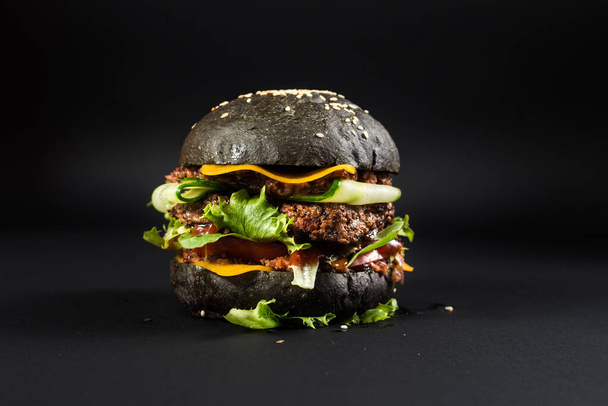 Tasty craft burger with black bun on the black background - Foto, afbeelding