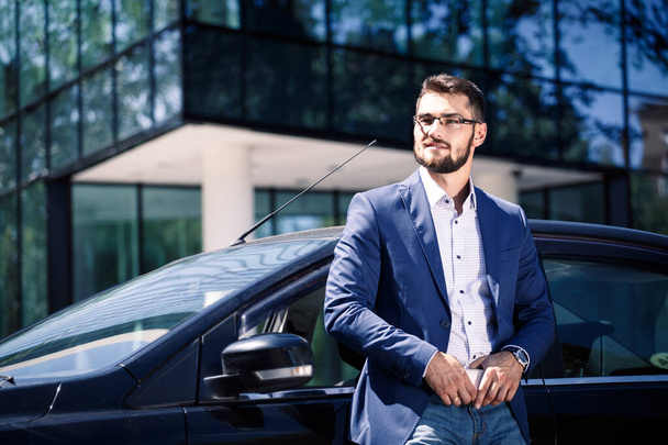Επιχειρηματίας στέκεται κοντά στο αυτοκίνητο. Δημιουργία γραφείων στο παρασκήνιο - Φωτογραφία, εικόνα