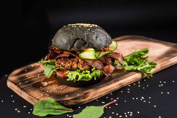 Tasty craft burger with black bun on the black background - Foto, Bild
