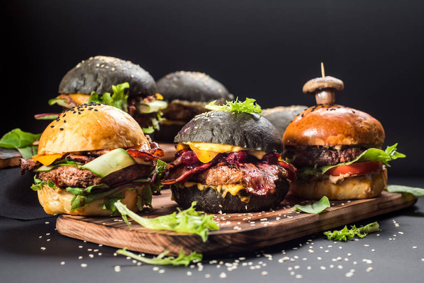 Assorted craft burgers with different fillings, with sesame seeds on the black background - Foto, Bild