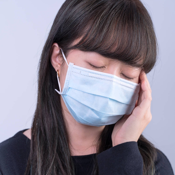 Young woman is feeling dizzy, headache, sick, unwell with wearing a medical blue face mask over the gray background, close up, copy space. - Foto, Imagen