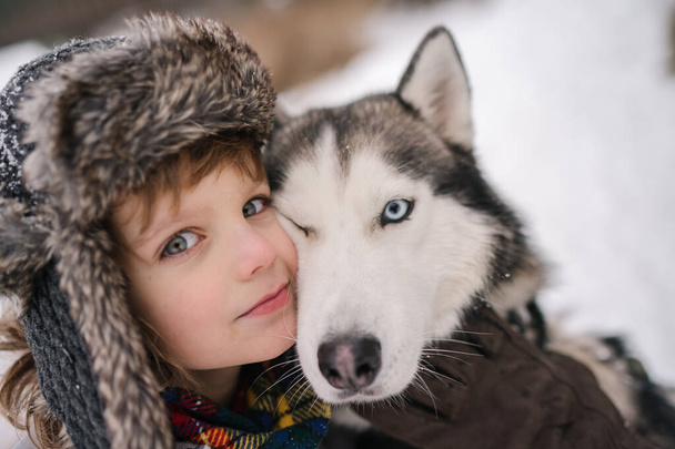 μικρό αγόρι με σγουρά μαλλιά αγκαλιάζει σιβηρικό κοπρόσκυλο  - Φωτογραφία, εικόνα