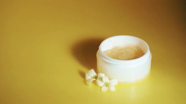 Cosmetische achtergrond voor productpresentatie. Gel-crème in witte pot met jasmijnbloemen op gele achtergrond. Motion schaduw van palmblad. - Video