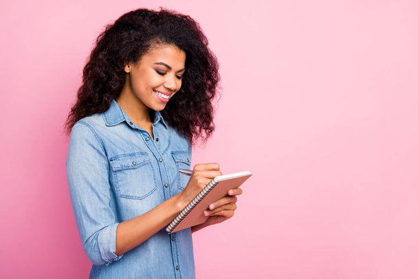 Πορτρέτο του θετικού επικεντρώθηκε αφρο Αμερικανός φοιτητής κορίτσι κολέγιο γράφουν βιβλίο αντίγραφο πανεπιστημιακή διάλεξη φορούν casual στυλ denim πουκάμισο απομονώνονται σε ροζ φόντο χρώμα - Φωτογραφία, εικόνα