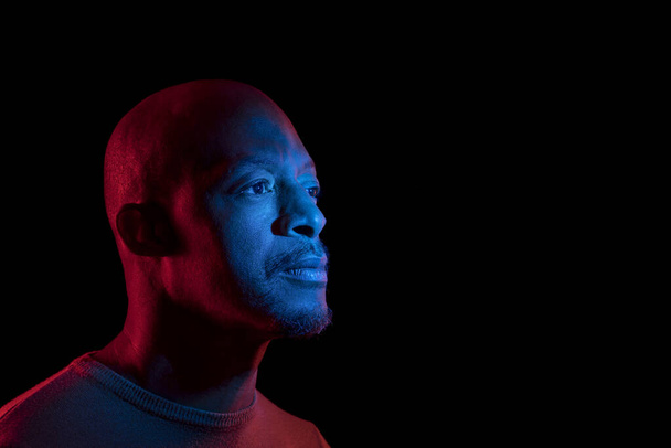 Uomo nero con luce blu e rossa, isolato su sfondo nero, guardando lateralmente. Copyspace
 - Foto, immagini