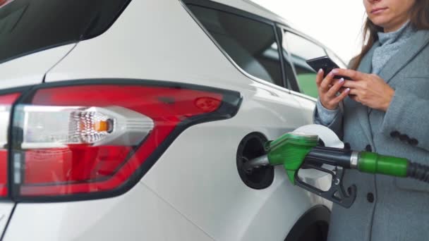 Woman using smartphone while her car is refueling. Slow motion - Footage, Video