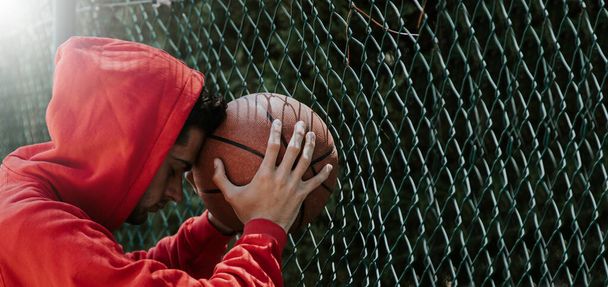 young teenage boy leaning on basketball ball outdoors - Fotó, kép