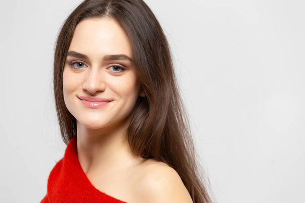 明るい灰色の背景に赤いセーターを着た明るい笑顔の若い美しい女性の肖像画 - 写真・画像