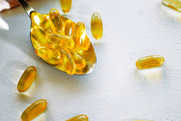 Tablespoon holding omega 3 cod liver oil supplement capsules on a white table top with copy space - Photo, Image