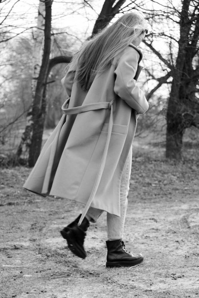 Outdoors lifestyle fashion portrait of happy stunning blonde girl. Beautiful smile. Long light hair. Wearing stylish coat. Joyful and cheerful woman. walk on a natural landscape, near a dry reed and a lake. black and white - Fotografie, Obrázek