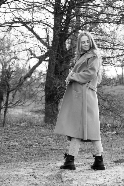 Outdoors lifestyle fashion portrait of happy stunning blonde girl. Beautiful smile. Long light hair. Wearing stylish coat. Joyful and cheerful woman. walk on a natural landscape, near a dry reed and a lake. black and white - Valokuva, kuva