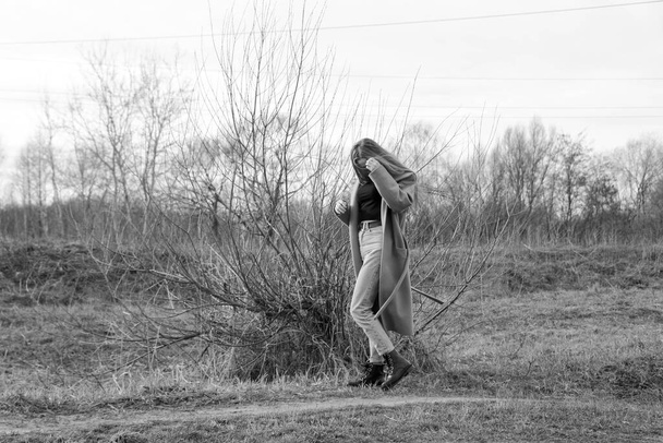 Outdoors lifestyle fashion portrait of happy stunning blonde girl. Beautiful smile. Long light hair. Wearing stylish coat. Joyful and cheerful woman. walk on a natural landscape, near a dry reed and a lake. black and white - Photo, image