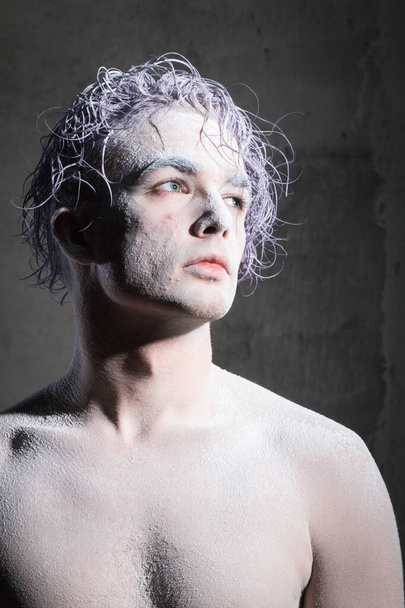 Male model in flour with purple hair on a gray background. Creative, unusual, vogue, glamor, purple hair, pose, fashion, art, artwork, beauty - Photo, Image
