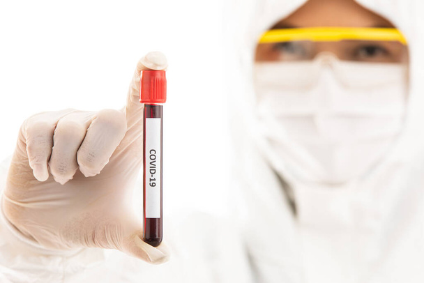 Steriliz laboratuvar önlüğü giyen bilim adamı elinde Covid-19 test tüpü örneği tutuyor. Virüsün adı üzerine seçici odaklanma. Coronavirüs 'ü yenmek için araştırma yapan tıp insanları için konsept. - Fotoğraf, Görsel