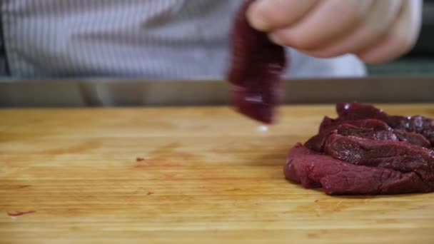 Chef cook in kitchen takes large fillet venison from an iron bowl and with knife cuts meat into pieces for dish, on wooden bamboo Board. Working as cook in kitchen of restaurant, preparing for dish. - Footage, Video