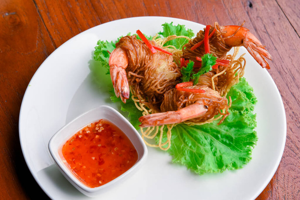 Goong Sarong nouilles Crevettes enveloppées avec nouilles croustillantes Servir, légumes et sauce dans une assiette blanche sur une table en bois, nourriture thaïlandaise - Photo, image