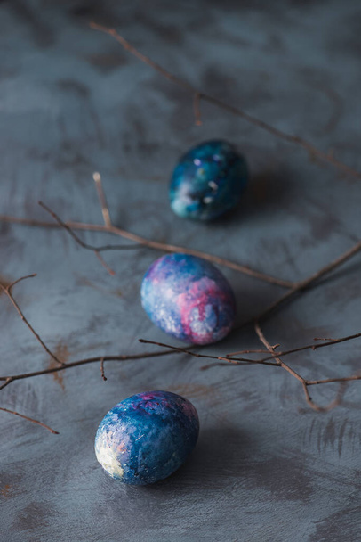 Paasvakantie. Pasen beschilderde kleurrijke eieren en tak. Blauwe achtergrond. - Foto, afbeelding