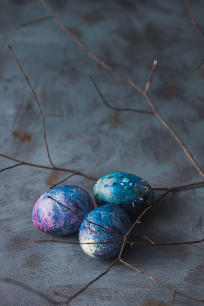 Concepto de vacaciones de Pascua. Huevos coloridos pintados de Pascua y rama sobre un fondo azul
. - Foto, Imagen
