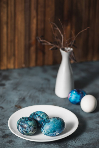 Easter still life. Easter eggs, a white plate and a white vase with dry branches. - 写真・画像