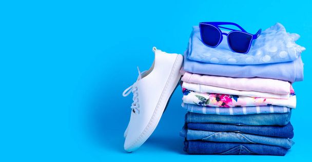 Stack folded colorful clothing summer, jeans and sunglasses, white sneakers - Foto, imagen