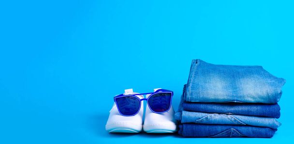 Stack folded jeans and sunglasses, white sneakers - Photo, image