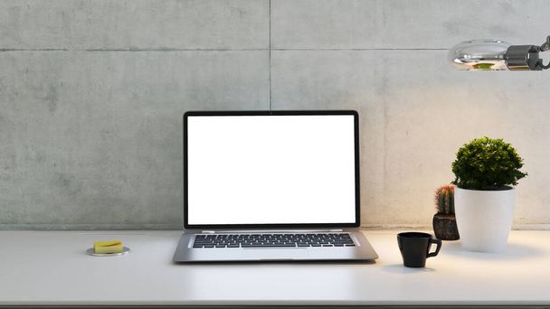 portátil en el escritorio con la planta, lámpara de escritorio, taza de café y la pared de hormigón 3D renderizado
 - Foto, imagen