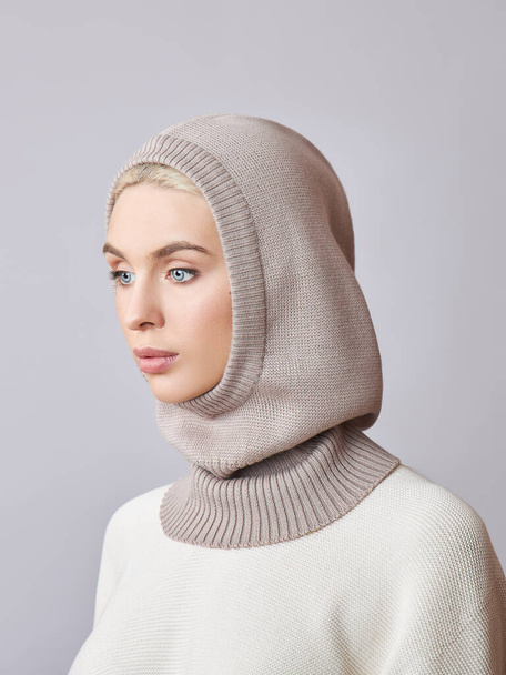 European Muslim woman with a blonde hair in a bonnet hood dressed on her head. Beautiful girl in sweater with soft skin, natural cosmetics - Fotoğraf, Görsel