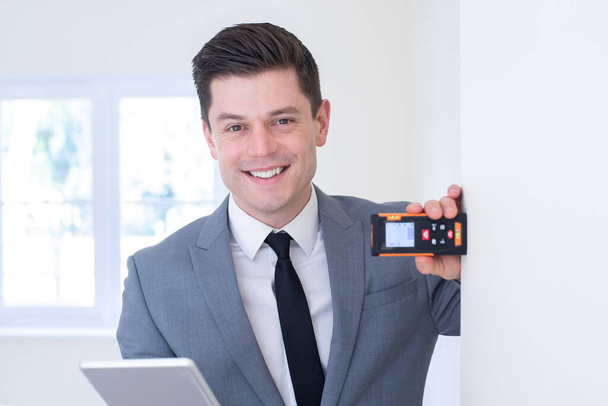 Portrait Of Male Realtor With Digital Tablet Measuring Room With Laser Measure - Photo, image